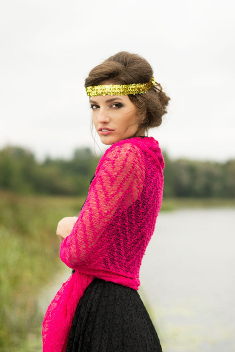 May include: A woman wearing a pink lace shawl over a black dress. She is wearing a gold headband and has her hair pulled back.