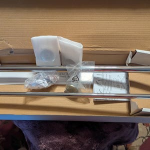Puede incluir: Un nuevo juego de toallero cromado, parcialmente montado, dentro de una caja de cartón. El kit incluye herrajes de montaje, instrucciones y dos piezas de plástico blanco. El toallero tiene un diseño de doble barra.
