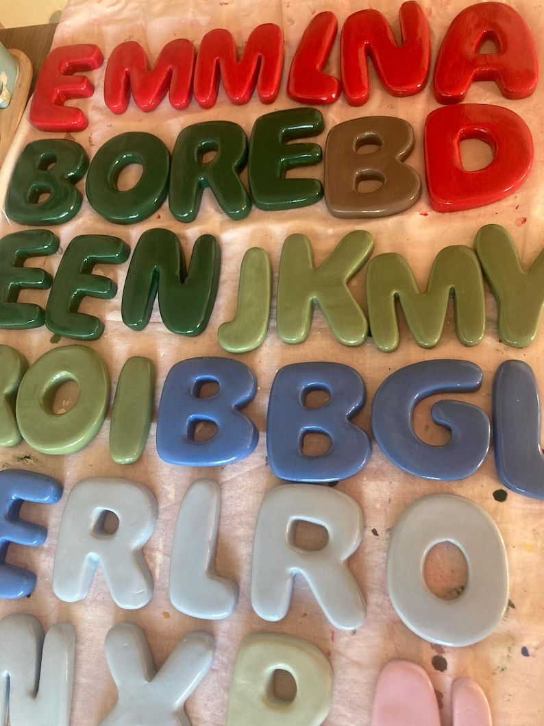 May include: A collection of colorful, glossy, 3D letters in various shades of red, green, brown, blue, and gray. The letters are arranged in rows, spelling out names and words. The letters are likely for decorative purposes.