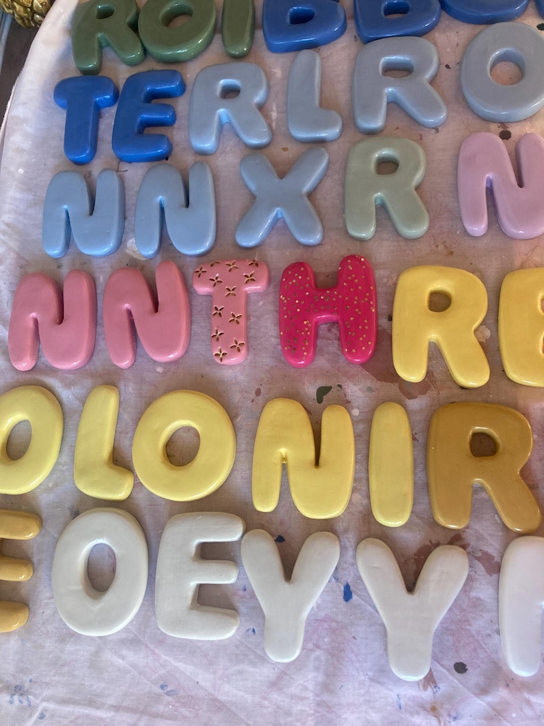 May include: A collection of colorful, bubble-style letters in various shades, including blue, pink, yellow, and green. The letters are arranged in rows, with some spelling out words. The letters have a glossy finish and are likely made of a hard material.