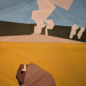 May include: Abstract textile art piece with geometric shapes. The design features a light blue sky, a dark green horizon, and a yellow foreground. White and brown shapes are incorporated, creating a unique, modern aesthetic. The piece is likely a quilt or fabric art.