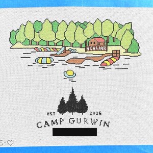 Op de afbeelding: Naaldkunst canvas met een kampeersc&egrave;ne aan het meer met bomen, water en een hut. De tekst "ACALIAH" staat boven het water. Hieronder staat de tekst "EST 2026 CAMP GURWIN" met een silhouet van bomen.