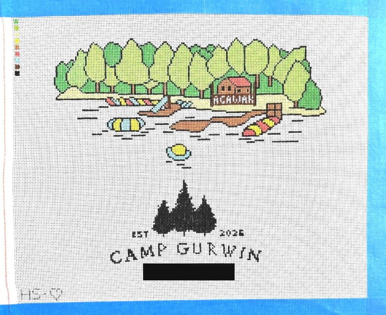 Op de afbeelding: Naaldkunst canvas met een kampeersc&egrave;ne aan het meer met bomen, water en een hut. De tekst "ACALIAH" staat boven het water. Hieronder staat de tekst "EST 2026 CAMP GURWIN" met een silhouet van bomen.