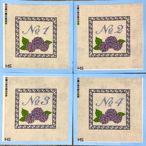 Op de afbeelding: Vier vierkante borduurkaders met lichtblauwe randen. Elk kader heeft een omlijnd ontwerp met een nummer, een tros paarse bloemen en groene bladeren. De nummers zijn "No 1", "No 2", "No 3" en "No 4".