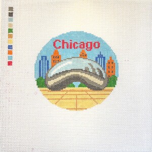 Op de afbeelding: Een borduurontwerp met de skyline van Chicago, inclusief de iconische Cloud Gate-sculptuur. Het woord "Chicago" is rood boven de sculptuur gestikt. De achtergrond is een lichtblauwe cirkel met oranje en blauwe gebouwen.