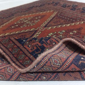 May include: A woven rug featuring a deep terracotta orange and dark navy blue color palette. The textile displays intricate geometric patterns, including diamonds and repeating border motifs, with a folded corner revealing the thick pile texture.