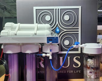 May include: A water filtration system with clear cylindrical housings and white components. The system includes multiple filters, tubing, and a digital display. The background features a gray panel with a logo and the text "WATERED FOR LIFE."