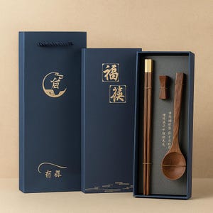 May include: A dark blue gift box set containing wooden chopsticks, a spoon, and a chopstick rest. The box has gold Chinese characters and a matching gift bag. The chopsticks have gold accents.