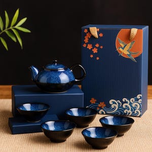 May include: A ceramic tea set in blue and black, comprising a teapot and four bowls. The set is presented with a gift box decorated with a bird and floral motifs. The teapot has a black handle and lid.
