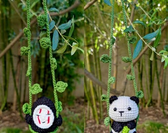 May include: Two crochet ornaments hanging from a tree branch. One is a black figure with a white face and red markings, the other is a panda bear. Both are suspended by green vines with leaf accents.