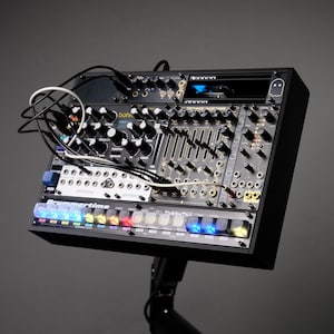 Könnte beinhalten: Schwarzes elektronisches Musikproduktionsgerät mit zahlreichen Knöpfen, Schiebereglern und Anschlüssen. Das Gerät hat einen Bildschirm und eine Reihe mehrfarbiger beleuchteter Tasten. Der Text "Drummertime" ist sichtbar.