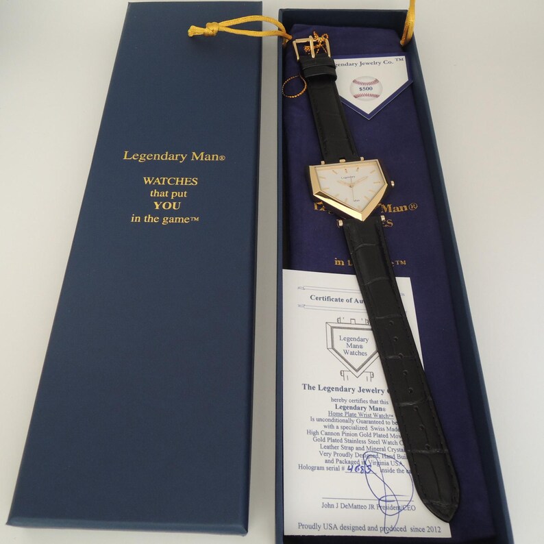 May include: A home plate-shaped wristwatch with a gold-tone case and a black leather strap, presented in a navy blue box. The box lid features the text Legendary Man WATCHES that put YOU in the game. Includes a certificate of authenticity.