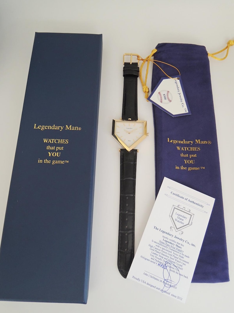 May include: A gold-tone triangular watch with a black leather strap, presented with a blue box, a blue drawstring pouch, a baseball-themed tag, and a certificate of authenticity. The box and pouch feature the text Legendary Man WATCHES that put YOU in the game.