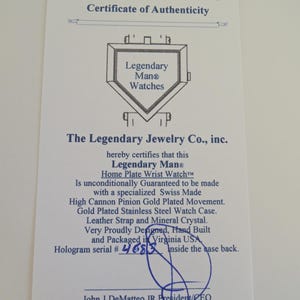 May include: A white Certificate of Authenticity for a Legendary Man Watches Home Plate Wrist Watch. The document features a line drawing of a home plate, blue text, and a handwritten hologram serial number 4683, signed by John J DeMatteo JR.
