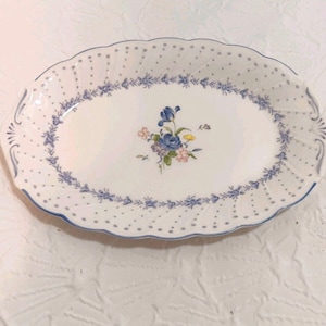 May include: Oval serving platter with a white base, decorated with a blue floral pattern and a delicate blue dotted border. The centre features a bouquet of blue, pink, and yellow flowers. The edges have a scalloped design.