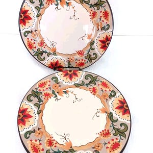May include: Two decorative ceramic plates with floral designs. The plates feature a cream-colored center surrounded by a gray border with red, orange, and green floral patterns. The rims are black.