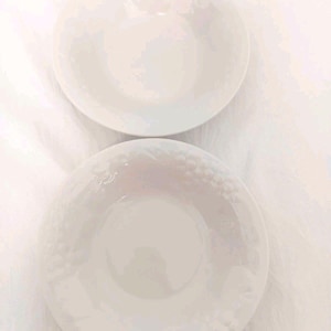 May include: Two white, round bowls. The bowls have a simple, elegant design, with a slightly textured surface. The bowls are likely made of ceramic or porcelain. The bowls are suitable for serving soups, salads, or other dishes.