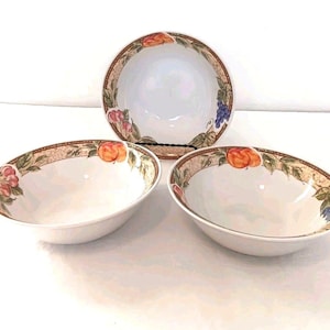 May include: Three white ceramic bowls with a fruit and vine design. The bowls have a wide rim with peaches, grapes, and leaves. The bowls are arranged on a white surface.