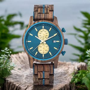 Peut inclure: Une montre-bracelet en bois avec un cadran bleu sarcelle et une lunette assortie. Le bracelet de la montre est en bois et comporte un affichage de la date à 3 heures. Le cadran de la montre présente des aiguilles et des marqueurs dorés.