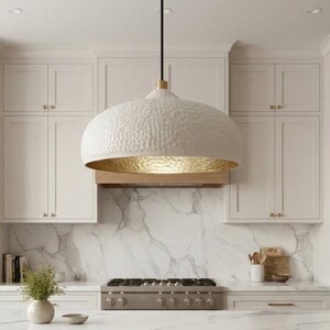 May include: A large, dome-shaped pendant light fixture with a textured matte white exterior and a metallic gold interior finish. The lamp is suspended by a thin black cord and features a small gold-toned cylindrical connector at the top.