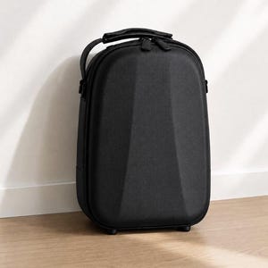 May include: A black, hard-shell carrying case with a handle and zip closure. The case has a textured surface and a geometric design on the front. It is standing upright on a wooden floor.