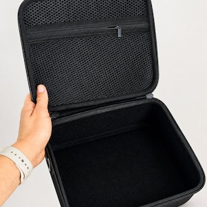 K&ouml;nnte beinhalten: Ge&ouml;ffnete schwarze Tragetasche mit einer Rei&szlig;verschluss-Netztasche im Deckel. Der Koffer wird offen gehalten und zeigt einen schwarzen Innenraum. Der Koffer hat einen schwarzen Rei&szlig;verschluss und ein schwarzes &Auml;u&szlig;eres.