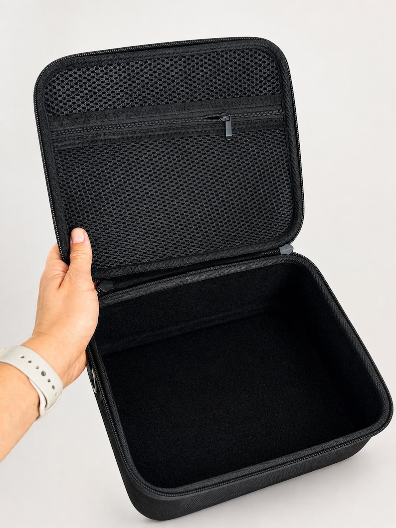 K&ouml;nnte beinhalten: Ge&ouml;ffnete schwarze Tragetasche mit einer Rei&szlig;verschluss-Netztasche im Deckel. Der Koffer wird offen gehalten und zeigt einen schwarzen Innenraum. Der Koffer hat einen schwarzen Rei&szlig;verschluss und ein schwarzes &Auml;u&szlig;eres.