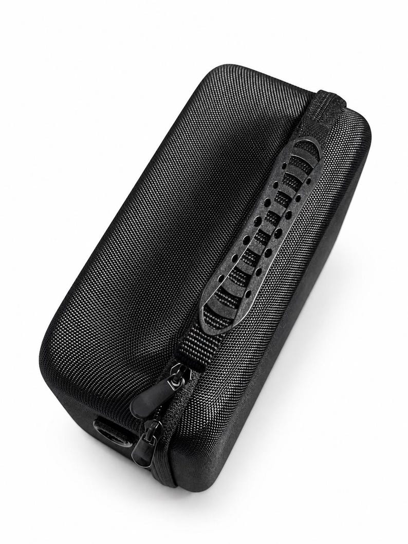 K&ouml;nnte beinhalten: Ein schwarzes, rechteckiges Etui mit strukturierter Oberfl&auml;che. Es verf&uuml;gt &uuml;ber einen schwarzen Rei&szlig;verschluss und einen Griff mit kleinen L&ouml;chern. Das Etui dient zum Schutz und Transport kleiner elektronischer Ger&auml;te oder Zubeh&ouml;rteile.