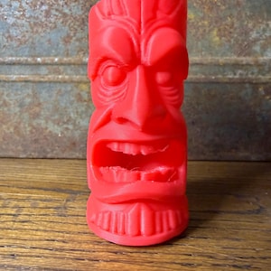 May include: A vibrant red tiki statue with a carved face, open mouth, and detailed features. The Polynesian-inspired sculpture is a solid, three-dimensional object, perfect for home decor or as a unique gift.