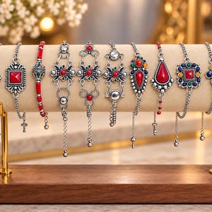 Peut inclure: Une collection de neuf bracelets argentés présentés sur un support cylindrique beige. Les bracelets présentent divers motifs avec des pierres rouges, bleues, vertes et jaunes, un travail du métal complexe et des chaînes délicates réglables.
