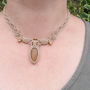 May include: A beige macrame necklace with a brown stone pendant and gold beads.