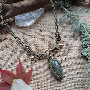 Puede incluir: Un collar de macramé verde con un colgante de piedra preciosa verde y rosa y detalles dorados.