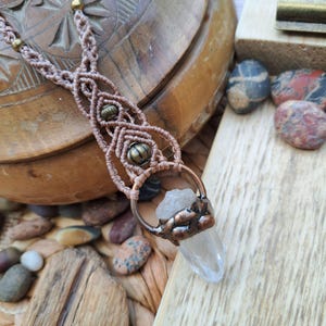 May include: A macrame necklace with a clear quartz crystal pendant wrapped in copper wire. The necklace features brown macrame cord and antique gold beads.