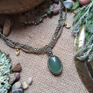 May include: A green stone pendant necklace with a macrame design and gold accents. The necklace is made with a green cord and features a large, oval-shaped green stone pendant.