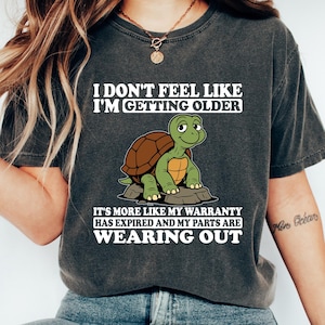 May include: Dark gray t-shirt with the text "I DON'T FEEL LIKE I'M GETTING OLDER" and a cartoon turtle. The shirt also says "IT'S MORE LIKE MY WARRANTY HAS EXPIRED AND MY PARTS ARE WEARING OUT".