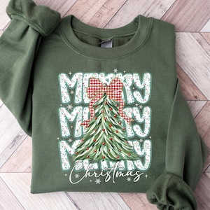 May include: Green sweatshirt with the words "MERRY MERRY MERRY Christmas" in white block letters. A Christmas tree with a red and white plaid bow is in the center. The sweatshirt has long sleeves and a crew neck.