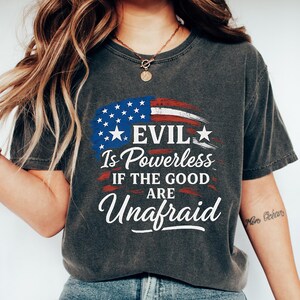 May include: Dark gray t-shirt with a distressed American flag design and the text "EVIL Is Powerless If The Good Are Unafraid" in white. The shirt is a casual style.