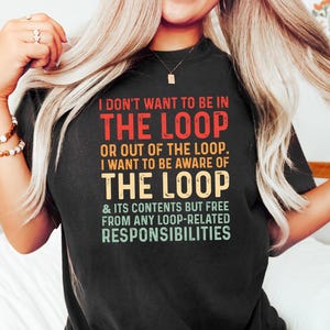 Puede incluir: Camiseta negra con el texto "I DON'T WANT TO BE IN THE LOOP" en rojo, verde y blanco. El mensaje de la camiseta continúa con "OR OUT OF THE LOOP. I WANT TO BE AWARE OF THE LOOP & ITS CONTENTS BUT FREE FROM ANY LOOP-RELATED RESPONSIBILITIES."