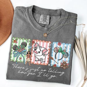 May include: A charcoal gray t-shirt featuring a graphic print of three rectangular panels with Moana, Pua the pig, and character-themed mouse ears. The text "There's just no telling how far I'll go" is printed in white script below the graphics.