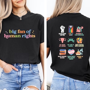 May include: Black t-shirt with the text "big fan of human rights" in colourful letters on the front. The back of the shirt features various graphics and phrases, including "Black Lives Matter" and "Trans Rights are Human Rights."