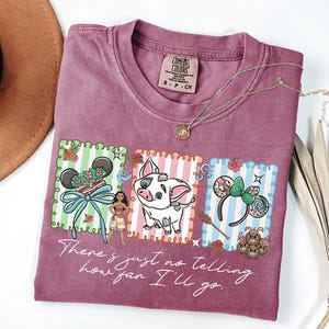 May include: A mauve short-sleeve t-shirt featuring a graphic print of Moana, Pua the pig, and themed mouse ears within three rectangular frames. The text "There's just no telling how far I'll go" is printed in white script below the illustrations.