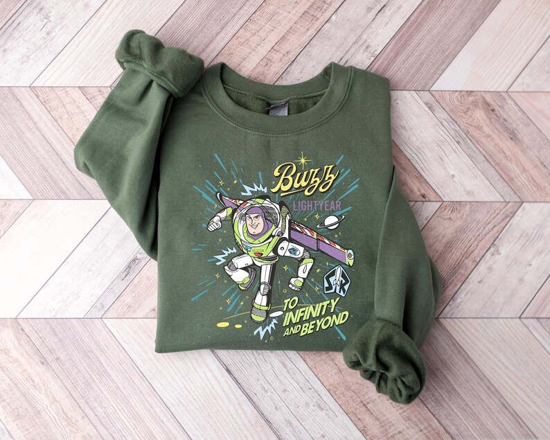 May include: Green crewneck sweatshirt featuring a graphic of Buzz Lightyear from Toy Story. The design includes the text "Buzz Lightyear" and "To Infinity and Beyond" with a space-themed background. The sweatshirt is made of a soft material.