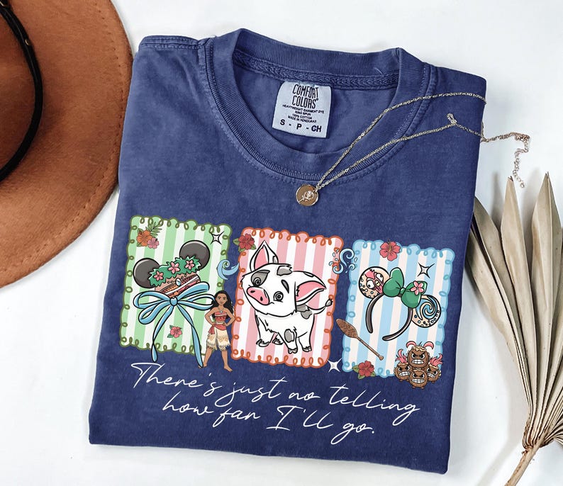 May include: A navy blue t-shirt featuring a graphic print of Moana, Pua the pig, and various themed icons within three rectangular frames. The text "There's just no telling how far I'll go" is printed in white script below the colorful illustrations.