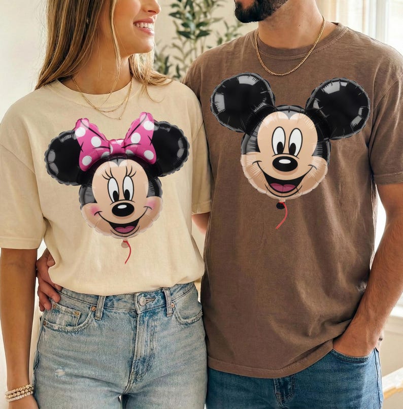 Peut inclure: Un t-shirt cr&egrave;me avec un motif de ballon Minnie Mouse portant un n&oelig;ud rose &agrave; pois et un t-shirt marron avec un motif de ballon Mickey Mouse. Les deux t-shirts ont des manches courtes et un col rond, mettant en valeur des personnages embl&eacute;matiques.