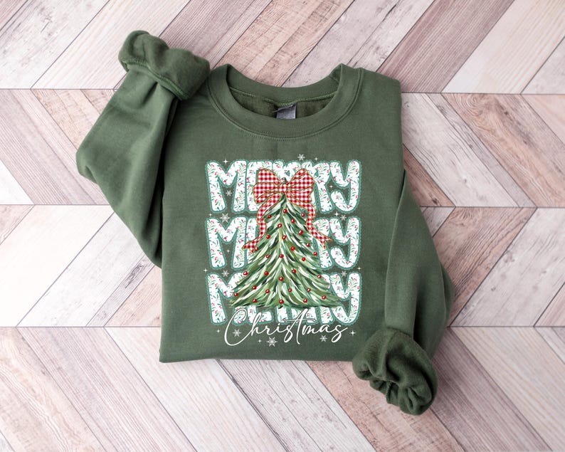 May include: Green sweatshirt with the words "MERRY MERRY MERRY Christmas" in white block letters. A Christmas tree with a red and white plaid bow is in the center. The sweatshirt has long sleeves and a crew neck.