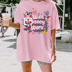 K&ouml;nnte beinhalten: Hellrosa T-Shirt mit dem Schriftzug "Walt Disney World" in einem farbenfrohen Design mit Mickey Mouse, Minnie Mouse, Donald Duck und Feuerwerk. Das Shirt hat eine lockere Passform.