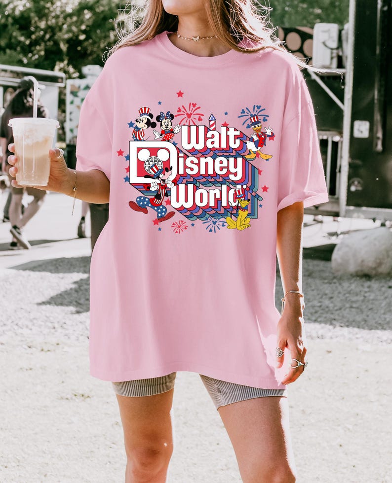 K&ouml;nnte beinhalten: Hellrosa T-Shirt mit dem Schriftzug "Walt Disney World" in einem farbenfrohen Design mit Mickey Mouse, Minnie Mouse, Donald Duck und Feuerwerk. Das Shirt hat eine lockere Passform.