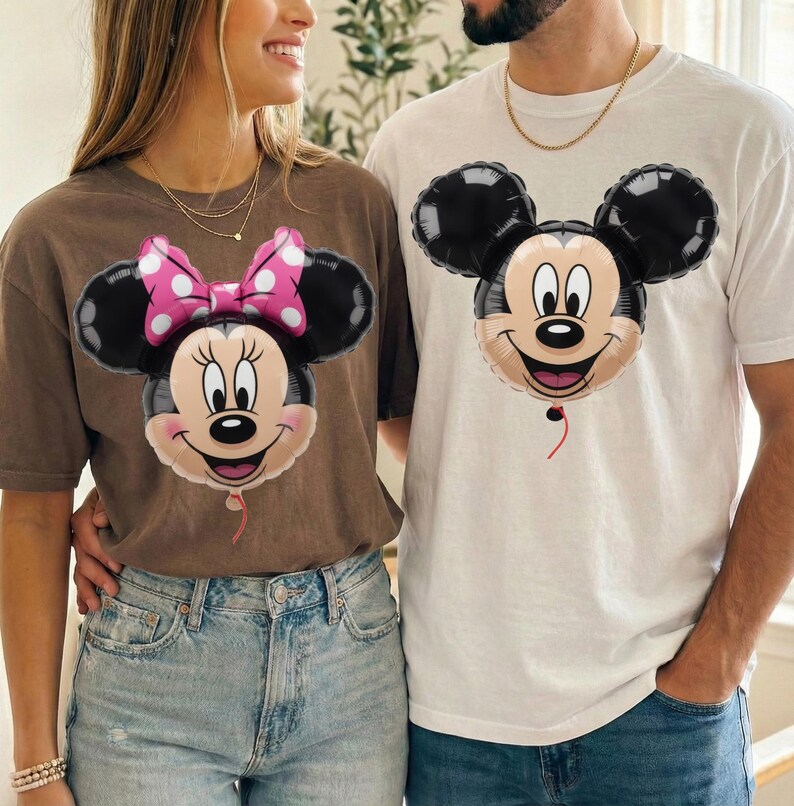 Peut inclure: Un t-shirt marron avec un motif de ballon Minnie Mouse portant un n&oelig;ud rose &agrave; pois et un t-shirt blanc avec un motif de ballon Mickey Mouse. Les deux t-shirts pr&eacute;sentent les visages des personnages sous forme d'illustrations de ballons gonfl&eacute;s.