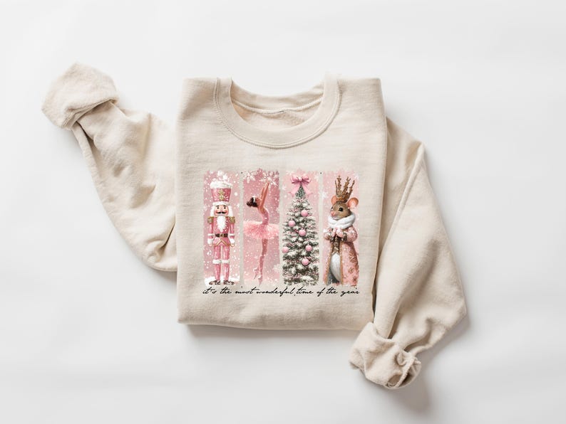 May include: Cream-colored sweatshirt featuring a festive design. The graphic includes a pink nutcracker, ballerina, Christmas tree, and a mouse in a crown. The text reads, "It's the most wonderful time of the year."