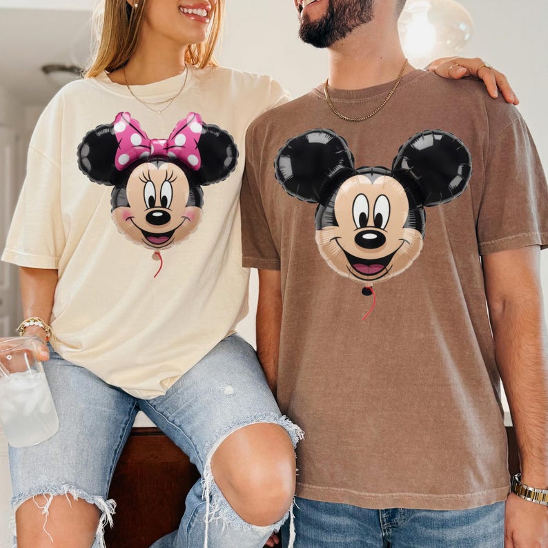Peut inclure: Un t-shirt cr&egrave;me avec un motif de ballon Minnie Mouse portant un n&oelig;ud rose &agrave; pois et un t-shirt marron avec un motif de ballon Mickey Mouse. Les deux t-shirts pr&eacute;sentent des manches courtes et une encolure ronde classique.